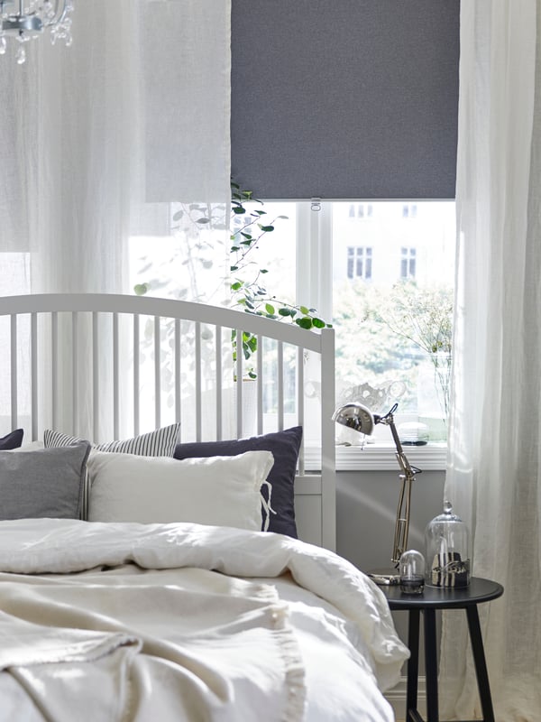 A bedroom with two FYRTUR block-out roller blinds, half-way down, in two windows above some chests of drawers.