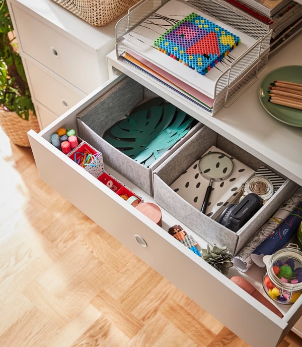 An open top drawer of a chest of drawers reveals paper and drawing accessories organised in KOMPLEMENT boxes.