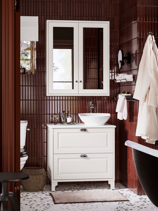 Dans une salle de bains carrelée bourgogne, un meuble lavabo à tiroirs TÄNNFORSEN et une vasque installés sous une armoire à pharmacie.