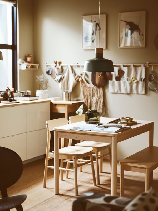 Una habitación de trabajo con muchas herramientas ordenadas en organizadores que cuelgan de una barra de madera. Al costado hay una mesa de madera con 3 sillas y sobre la mesa revistas y dos floreros.