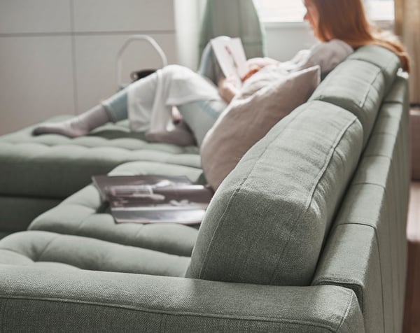 A person sitting in a light green LANDSKRONA sofa with a chaise longue.