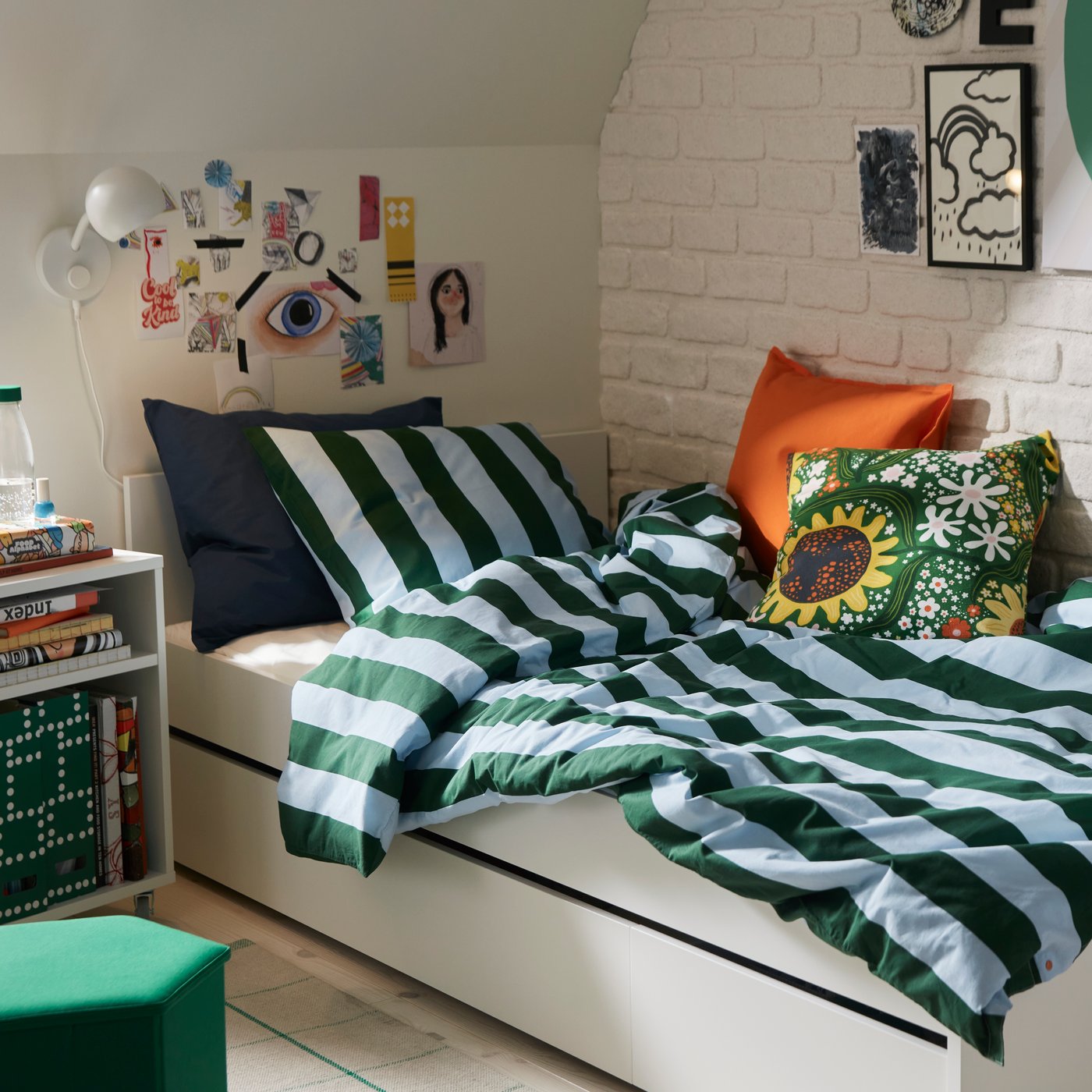 A bedroom with dark green and light blue striped SLÅNHÖSTMAL bedlinen on a white bed by a white brick wall.