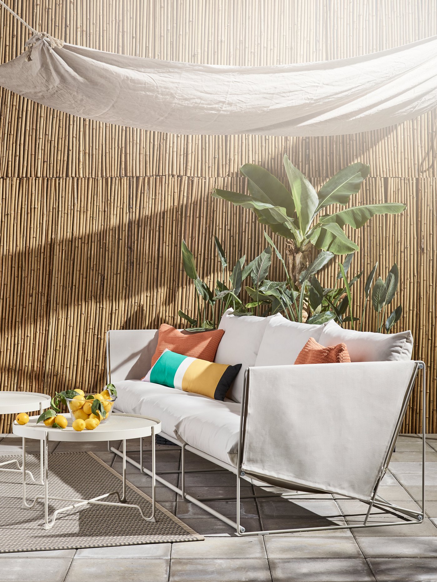Una terraza soleada con un sofá HAVSTEN con cojines de colores encima. Frente al sofá una mesa de centro con frutas encima.