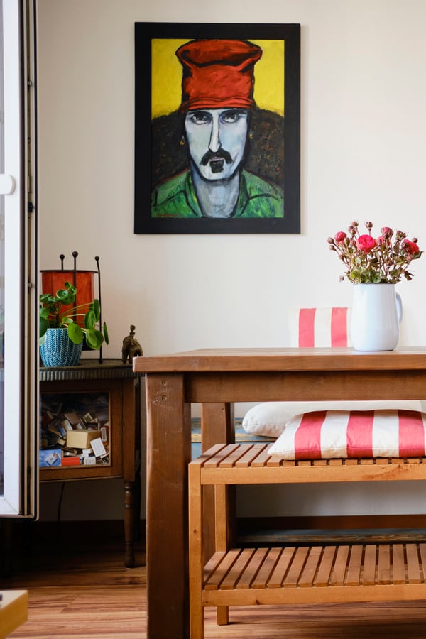 A clean dining area, with a solid wood table featuring flowers, a bench with cushions and a poster of Frank Zappa on the wall.