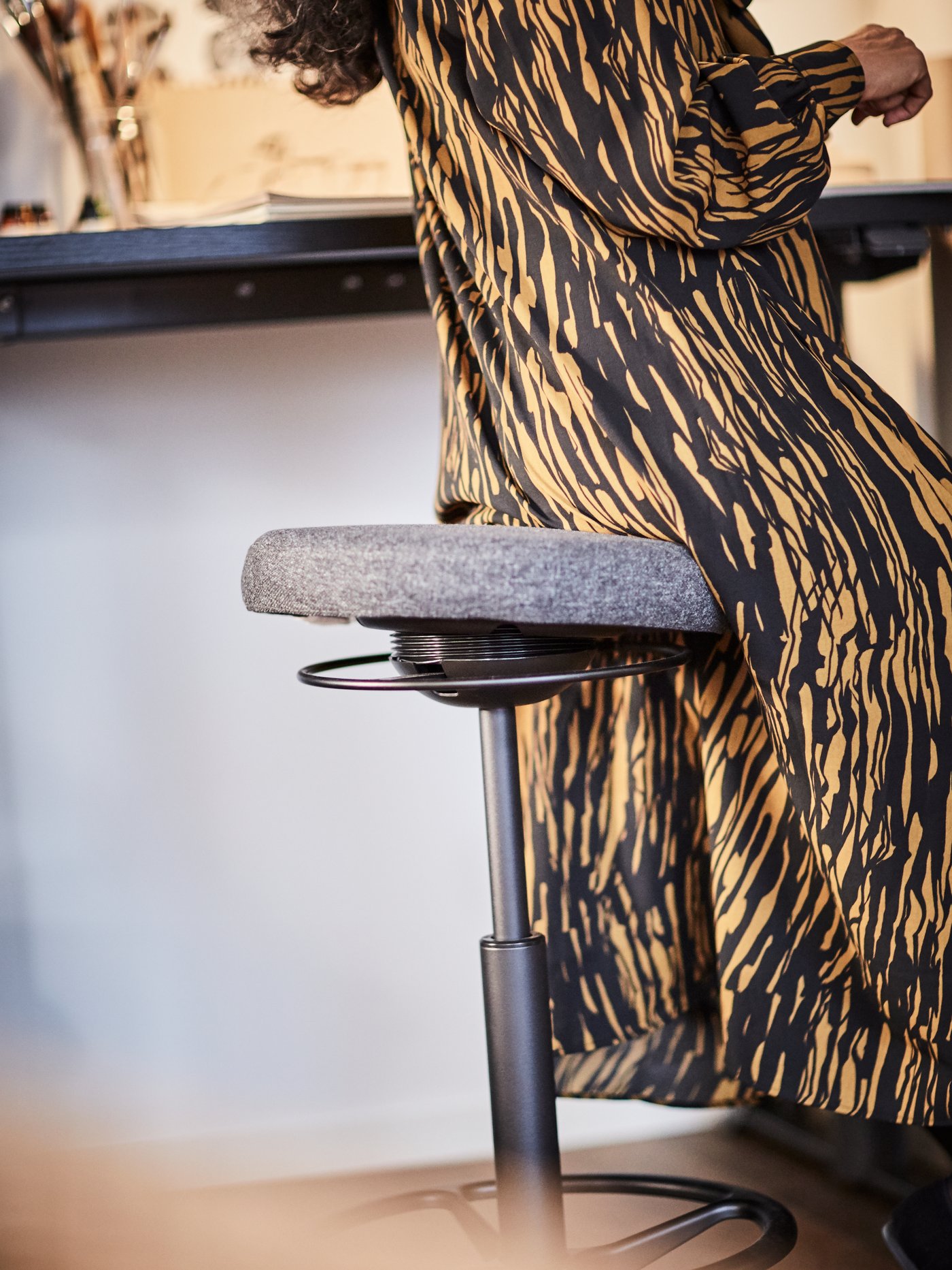 Woman in a patterned dress leaning on LIDKULLEN ergonomic stool.