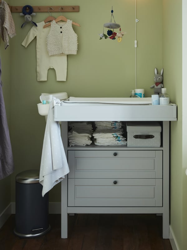 Section of a bedroom, half hidden behind a room-dividing curtain, with a baby’s cot and a SUNDVIK changing table.