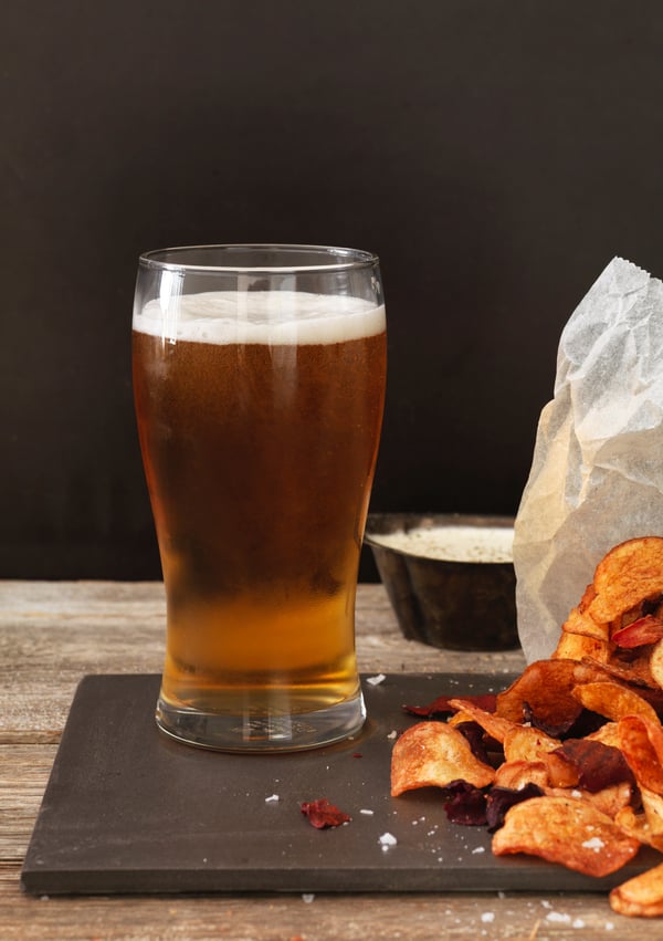 Un grand verre de bière dorée sur une table en bois, accompagné d'un tas de chips croustillantes et d'un petit bol de trempette.
