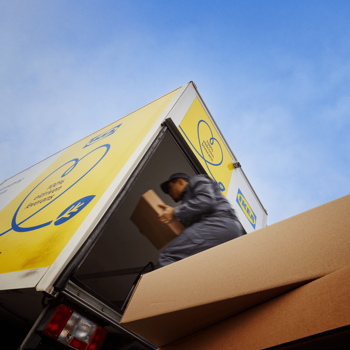 Zaposleni utovara kartonsku kutiju u IKEA kamion za isporuku pod vedrim nebom.