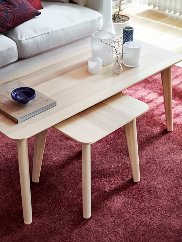 Mesa de centro LISABO bajo una mesa más grande de madera LISABO con velas sobre ella y un libro.