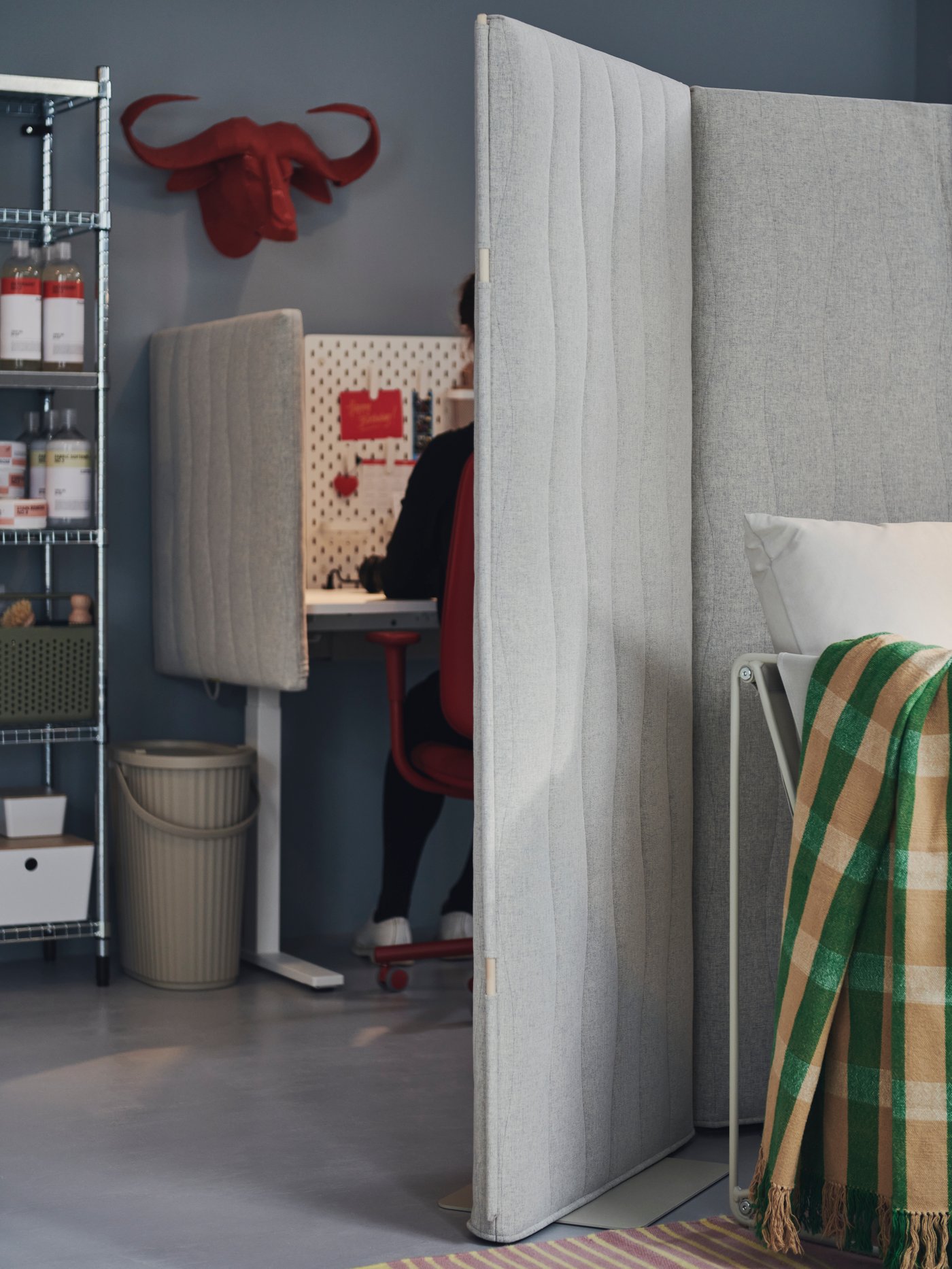 A person is sitting at a desk in a contemporary office. There is MITTZON acoustic screen behind, separating the space.