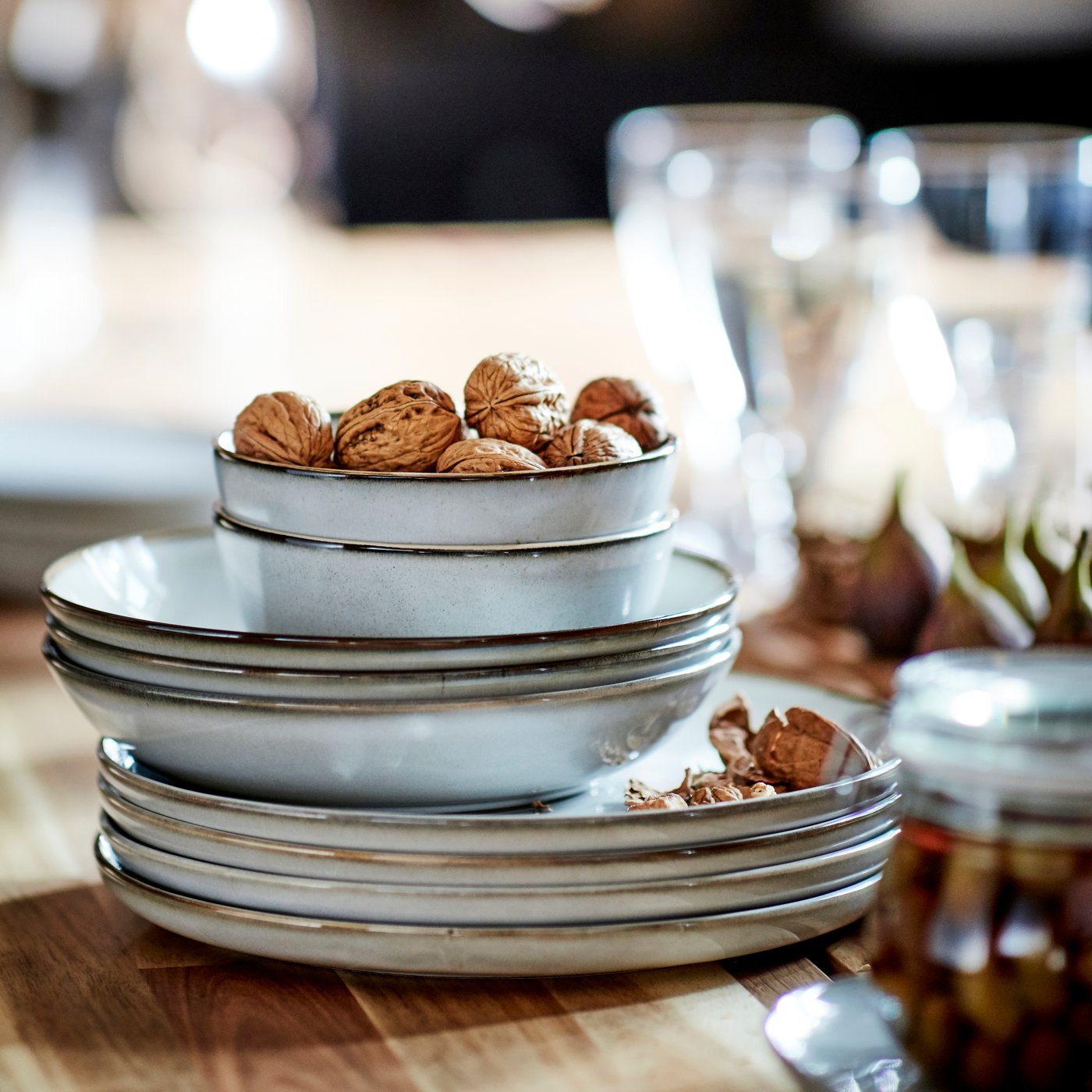 A stack of grey GLADELIG plates, side plates and bowls filled with walnuts on a set dining table.