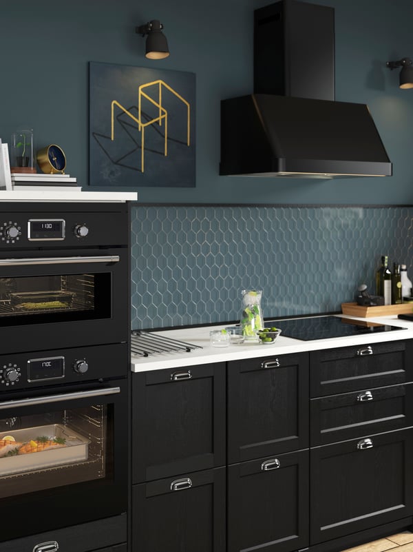 Eine schwarze Küche mit blauen Wänden, einem blauen Dunstabzug, einer weissen Arbeitsplatte und integrierter Mikrowelle und integriertem Backofen