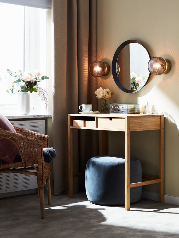 An armchair and a bamboo NORDKISA dressing table with a dark grey LANGESUND mirror mounted above it.