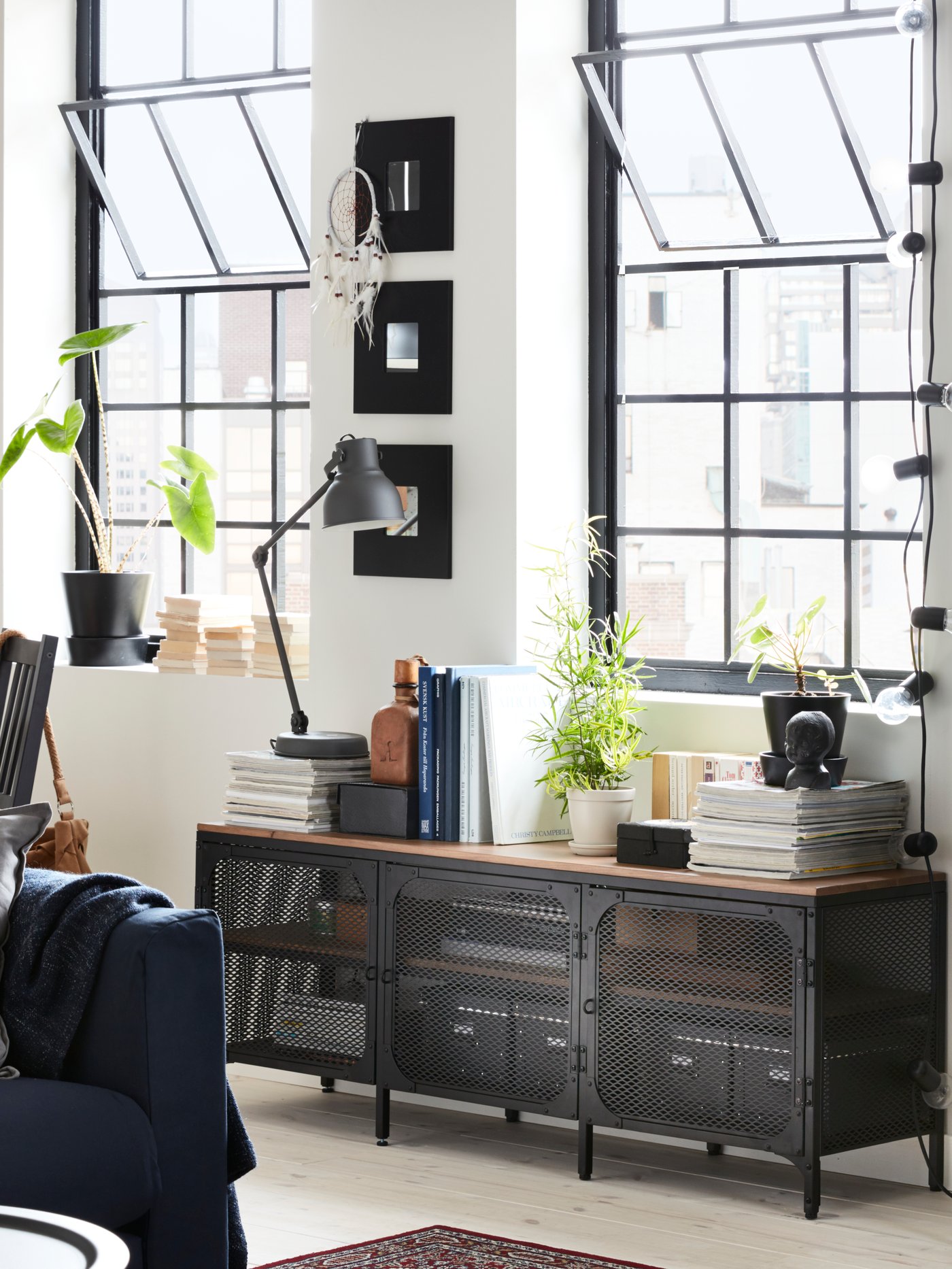 Meuble tv industriel en métal et bois avec livres et plante devant deux grands fenêtres