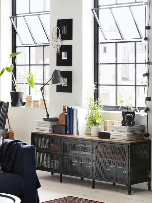 Buffet industriel en métal et bois, décoré de livres et plantes dans un salon au murs blancs et avec grandes fenêtres