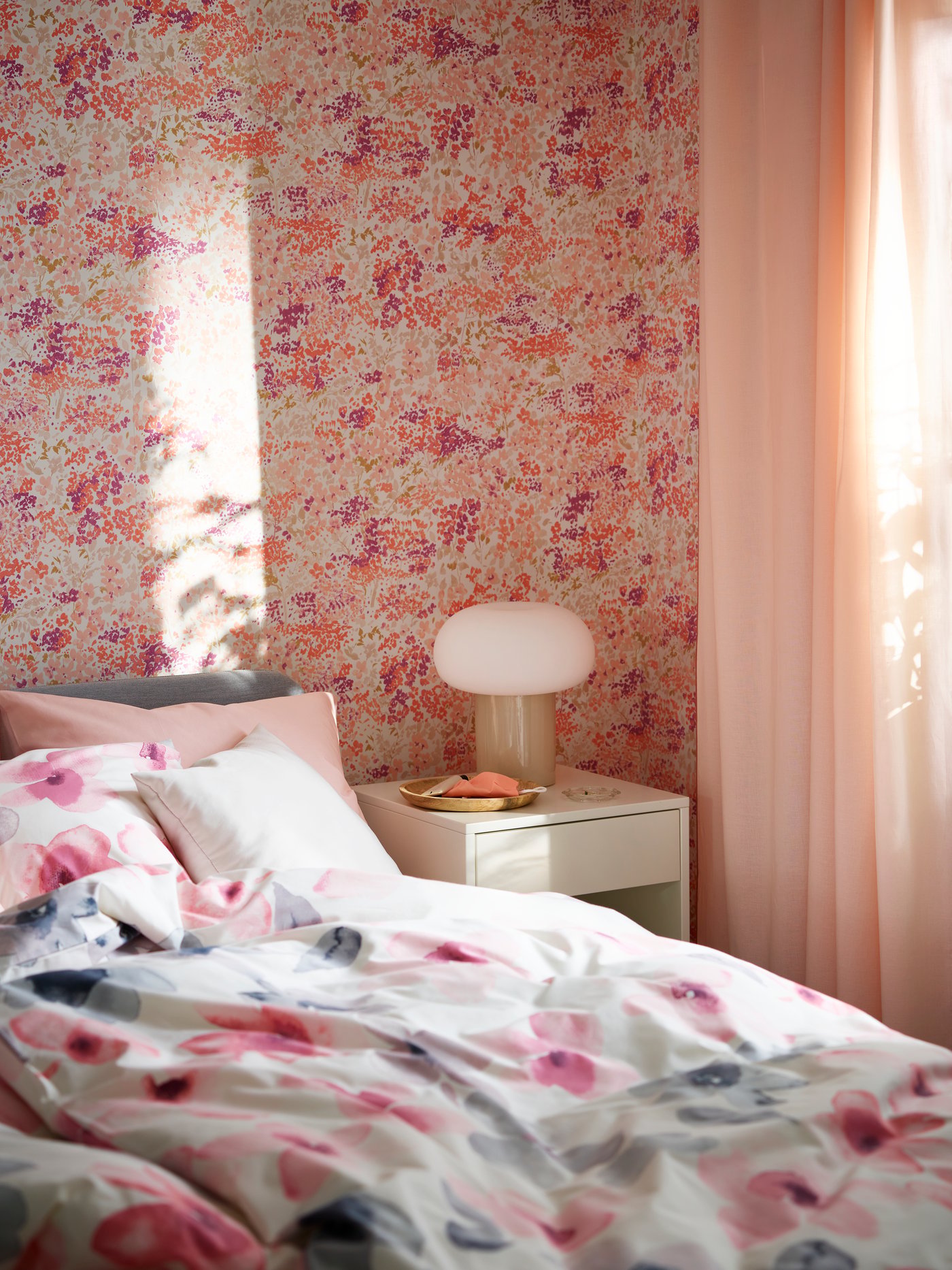 Vista de una habitación con papel mural floreado y una cama con sábanas floreadas en tonos rosas y azules con blanco.