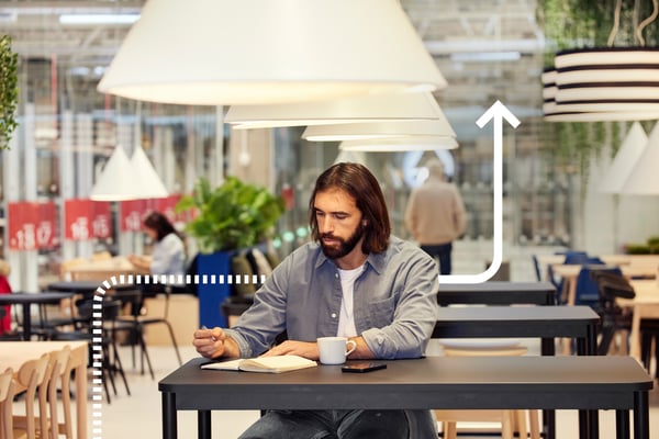 Un uomo seduto nel Ristorante Svedese di IKEA beve un caffè mentre scrive su un quaderno.