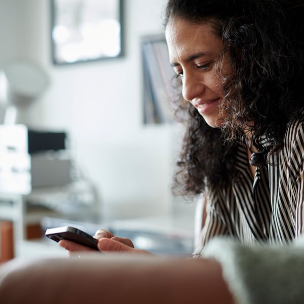 Une femme regarde son smartphone en souriant pendant qu’elle demande sa carte de crédit IKEA Family. 