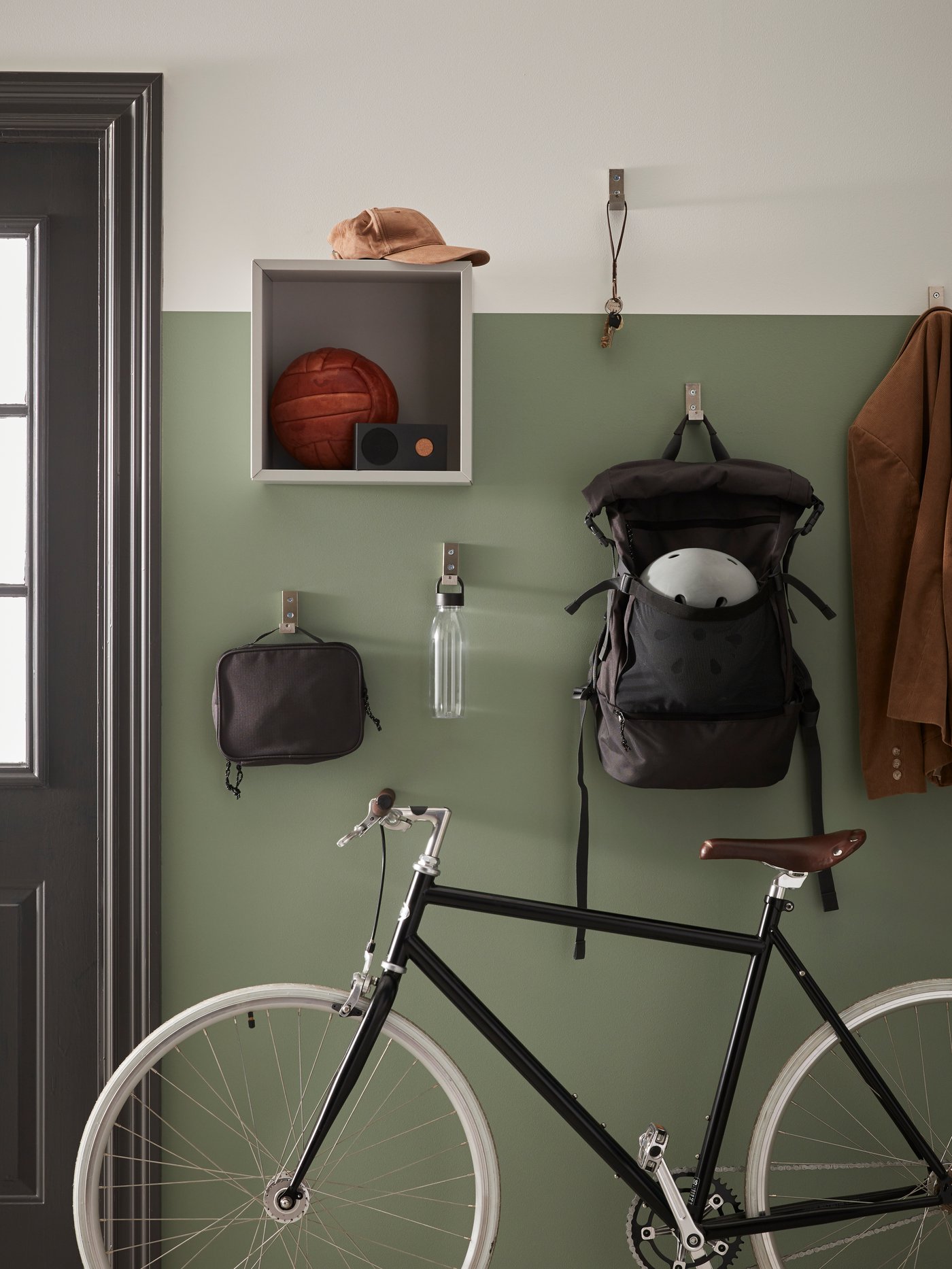 Una bicicleta en la entrada de una casa y sobre ella una repisa y ganchoscon ropa colgada.