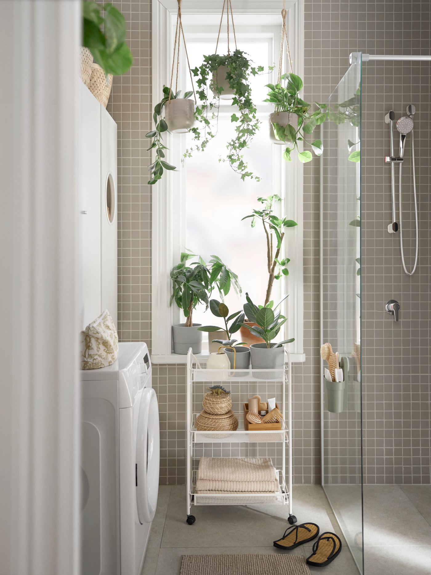 Baño con una lavadora UDDARP blanca, un carrito HORNAVAN blanco con varios artículos y un mueble de baño NYSJÖN blanco.