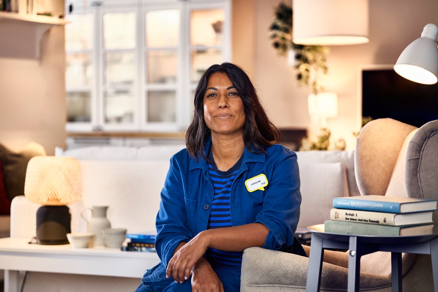 En IKEA-indretningsarkitekt iført sin blå arbejdsuniform sidder i et showroom og smiler til kameraet.