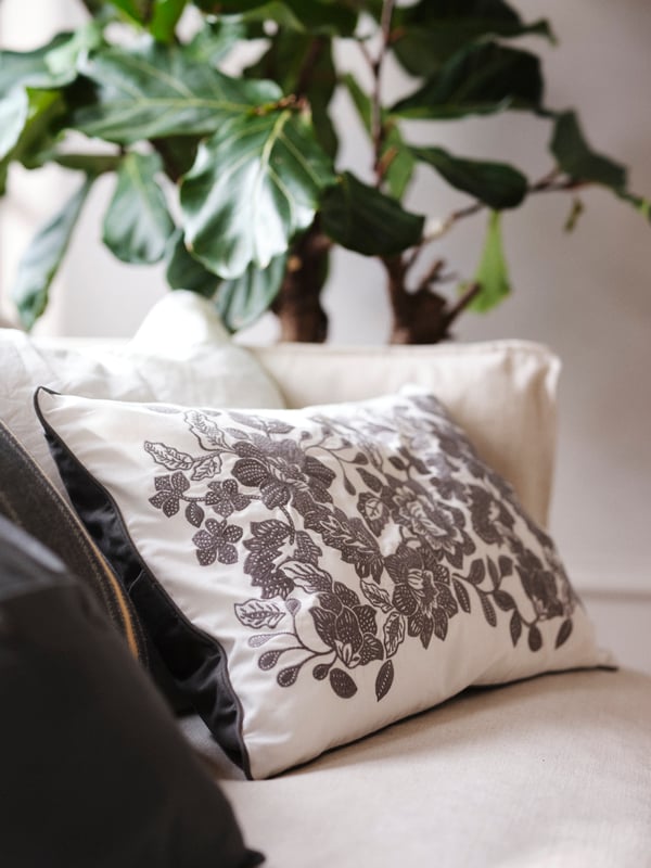 SKUGGNÄVA cushion cover with black floral print placed in a white sofa.