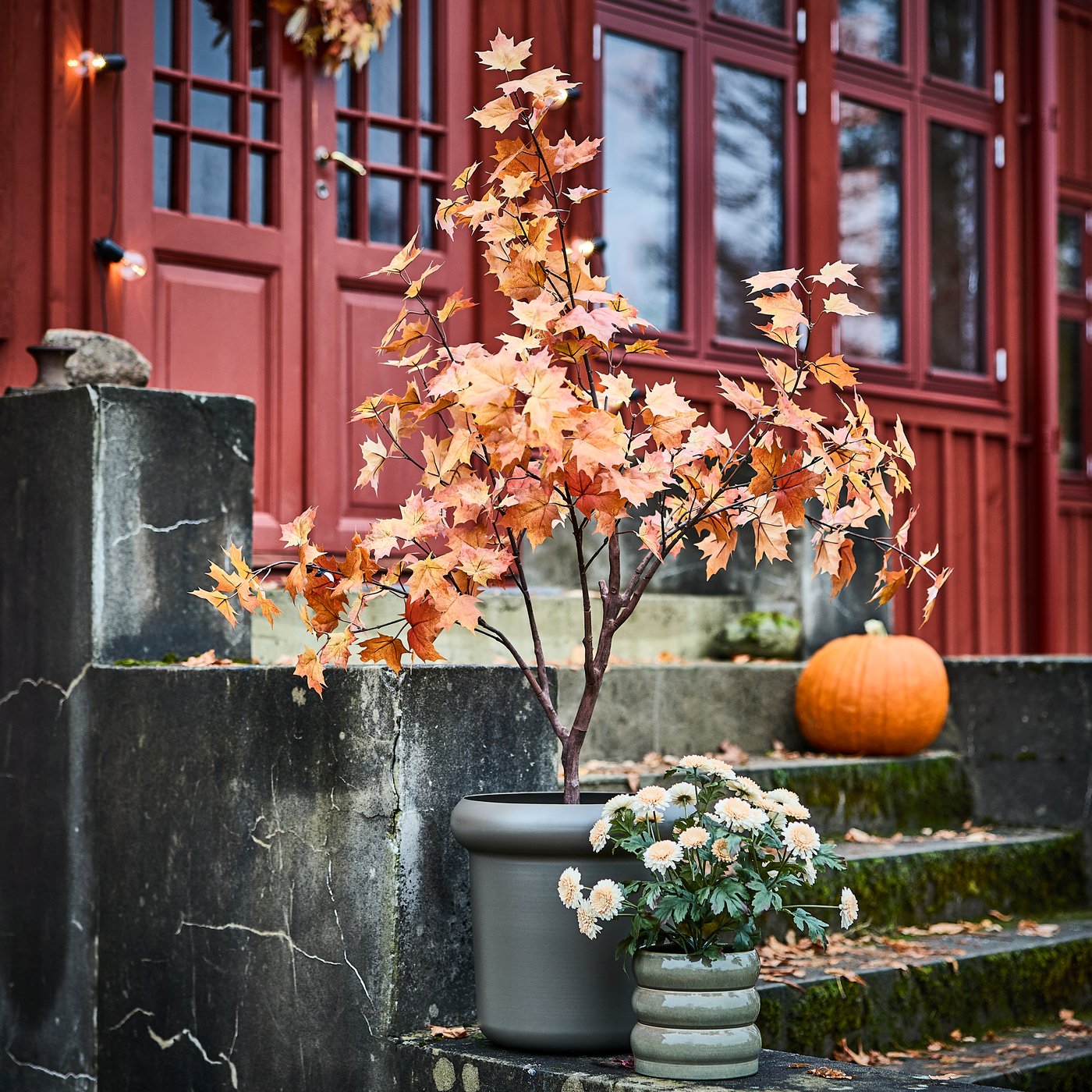 A FEJKA artificial maple tree in a MÅBÄRSBUSKE plant pot stands on an outdoor staircase next to smaller potted plant.