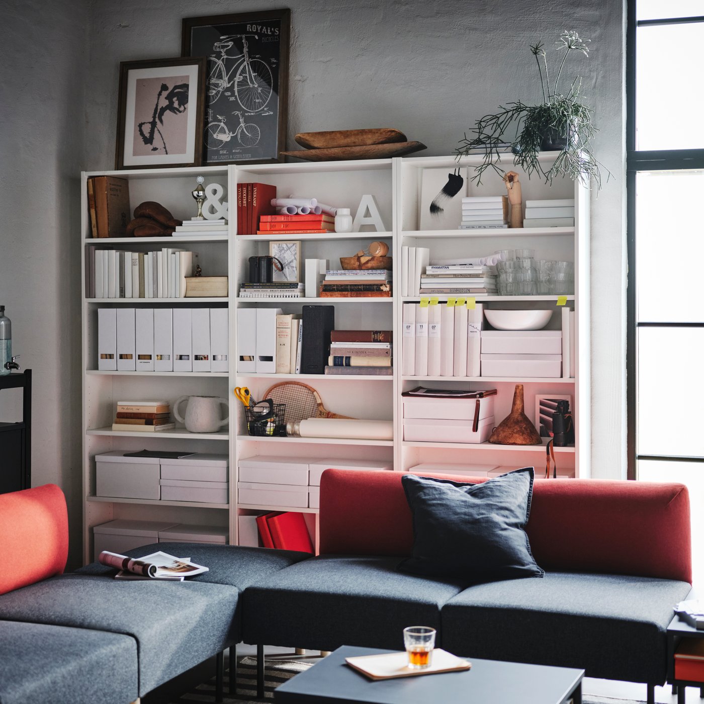 Three white BILLY bookcases with books, magazine files and other items, standing side by side in a living room.