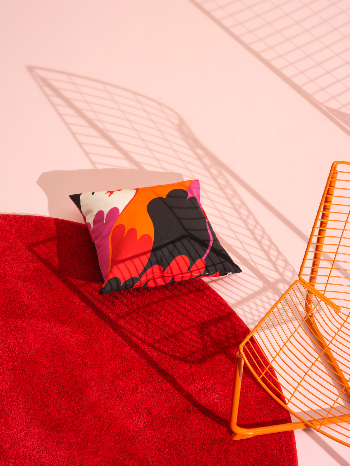A red circular rug sits on a white floor. A patterned pillow and orange chair sit on top.