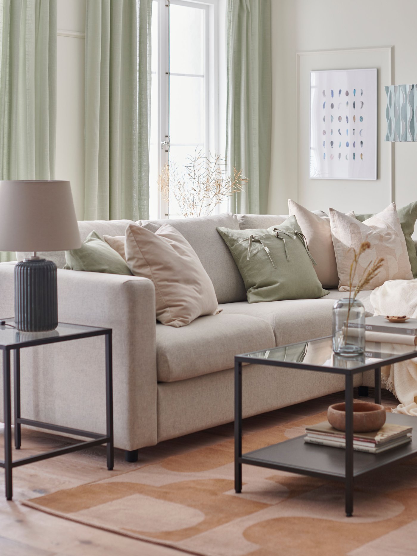 An IKEA VIMLE beige sofa in a living room with green curtains, black coffee and side tables and a pink rug.