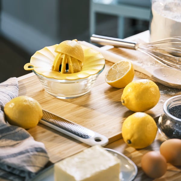 An UPPFYLLD lemon squeezer with half a lemon and an UPPFYLLD handheld grater, on an APTITLIG chopping board with lemons.