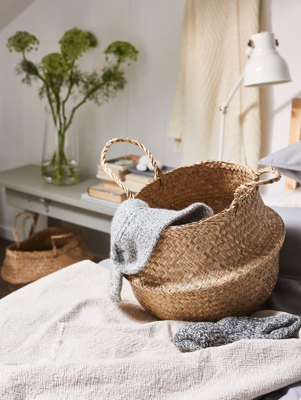 A FLÅDIS wicker basket sits on a organic bed linen, a work lamp sits in the background.