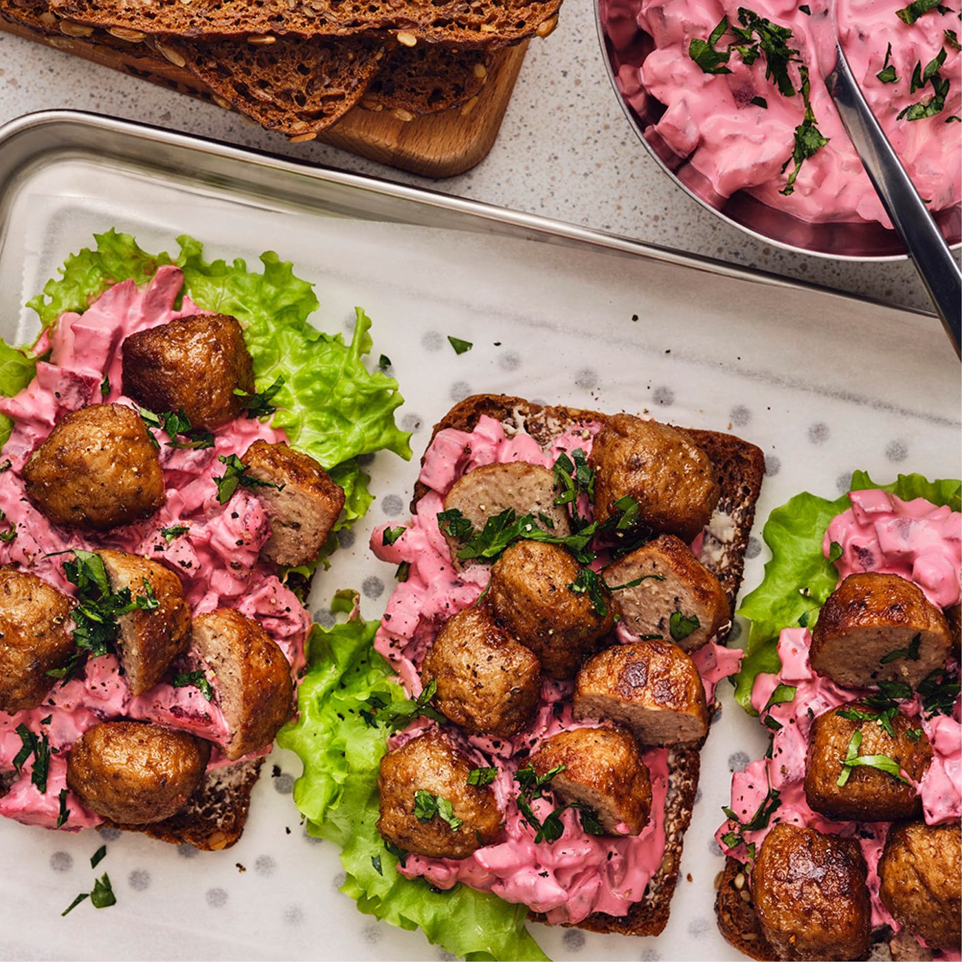 Tartines garnies de boulettes suédoises, salade de betteraves crémeuse et laitue verte, servies sur un plateau de pain de seigle.