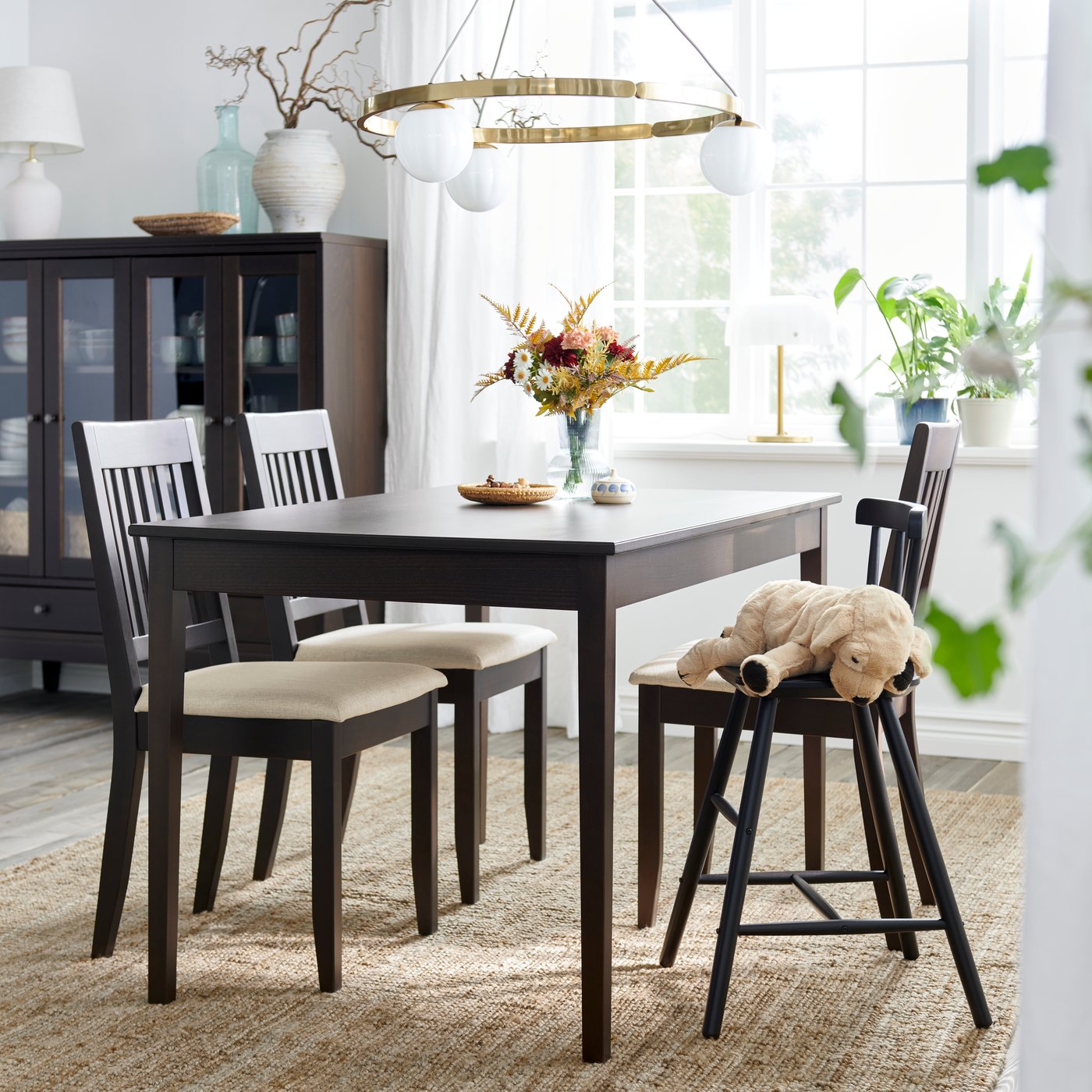 A dark brown NÄSINGE extendable table is set in a bright dining area with white chairs, flowers, and a pendant light.