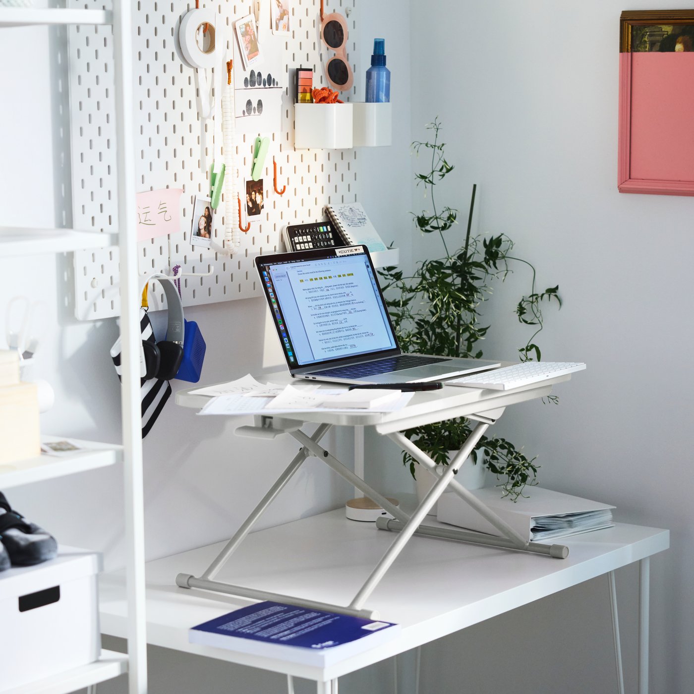 A white DUBBLA laptop stand with a laptop on top of it stands on a white desk next to a plant in a plant pot.