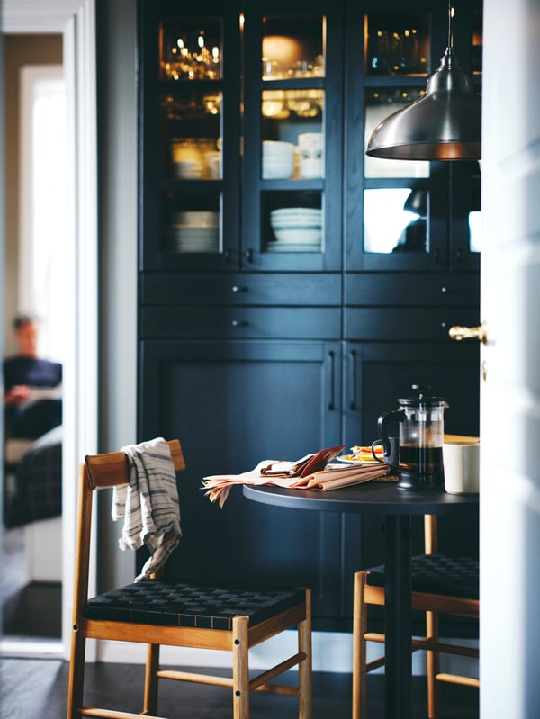 Kitchen cabinets with black stained LERHYTTAN doors behind an anthracite STENSELE table and two acacia NACKANÄS chairs.
