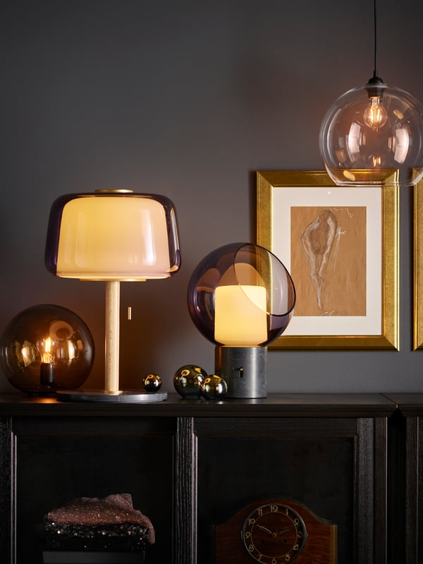 EVEDAL table lamp on top of a BESTA storage cabinet cupboard next to a FADO lamp. next to a few picture frames which are mounted on the wall.