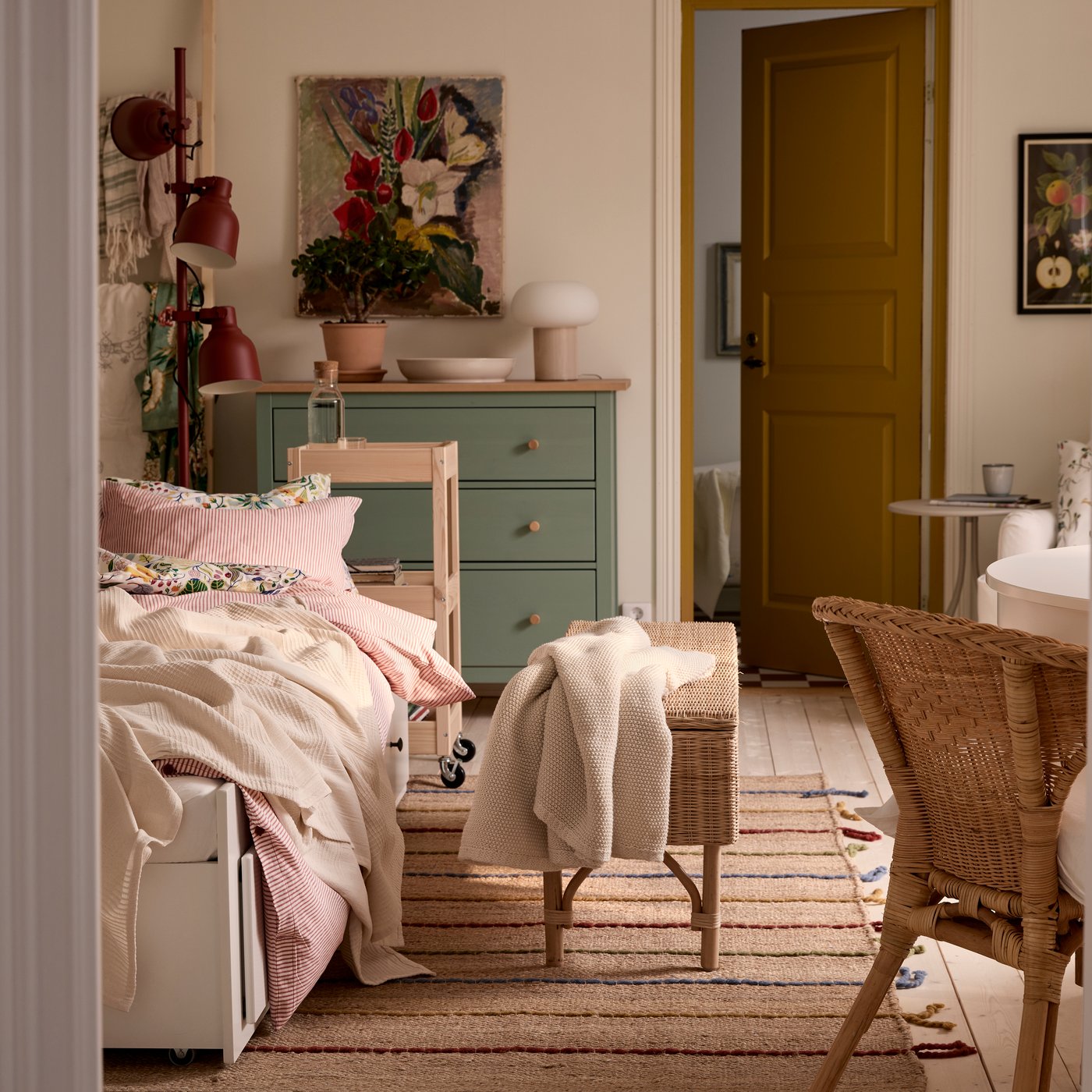 A one-bedroom apartment with HEMNES day-bed, a rattan chair in the foreground and a green HEMNES chest of drawers in the back.