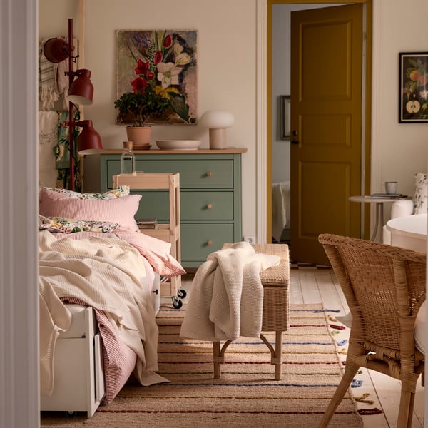 Jednosoban stan s HEMNES dnevnim krevetom, stolicom od ratana u prvom planu i zelenom HEMNES komodom s fiokama pozadi.