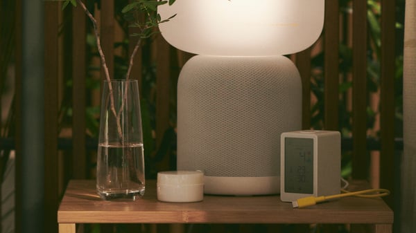 SYMFONISK lampa s Wi-Fi zvučnikom na stolu pored raznih ukrasa.