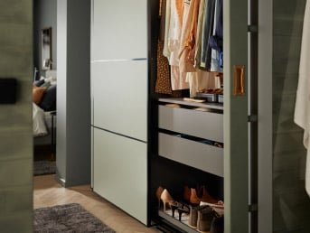 Une armoire PAX gris foncé/vert clair avec portes coulissantes dans la chambre.