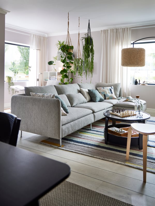 Sofa SÖDERHAMN berwarna kuning air/coklat dengan tumbuhan gantung di atasnya dan meja kopi BORGEBY berwarna hitam dengan permainan dan botol di atasnya.