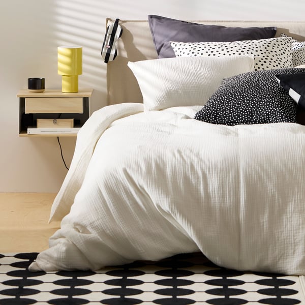 One side of a KLEPPSTAD bed covered with white SCHERSMIN bed linen with a STOMSÖ wall-mounted bedside table by it.