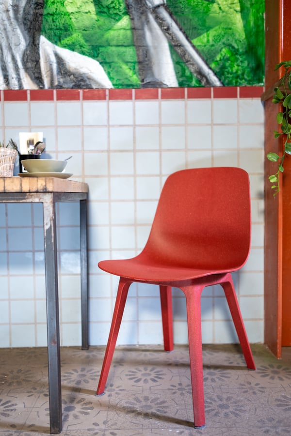 Een ODGER stoel in rood staat naast een eenvoudige tafel in een kleurrijke keukenhoek met tegels en planten.