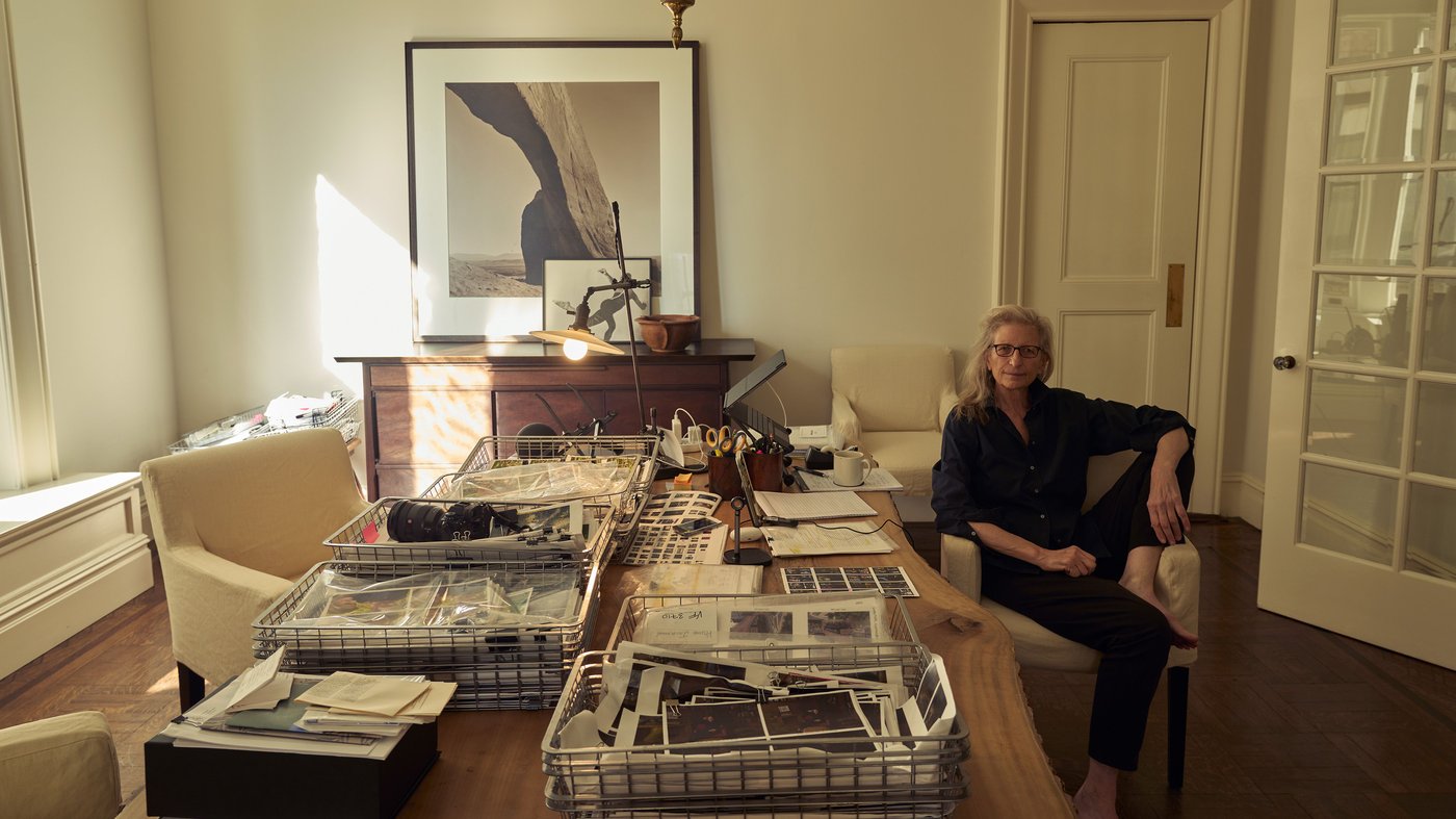 Annie Leibovitz sitting on a chair at a table full of things in his home.