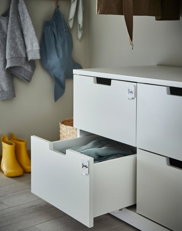 A chest of drawers and one drawer is open. The drawers have PLUTT hooks on them, and names are written here to help organise.