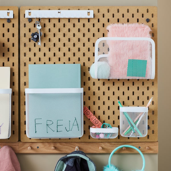 Kids’ belongings hang from HÖVOLM racks below SKÅDIS pegboards. The pegboards and racks form organised areas for children.