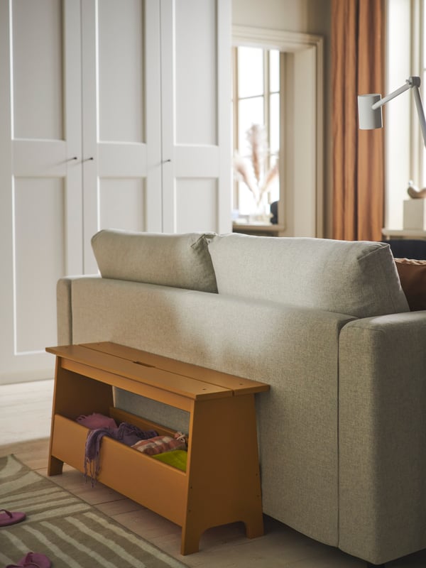 Un banc-coffre PERJOHAN avec rangement peint en ocre jaune est derrière une causeuse-lit VIMLE près d’une armoire-penderie PAX/GRIMO.