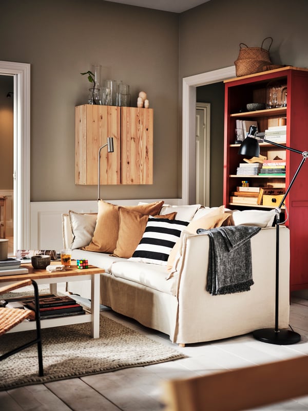 A living room with a BACKSÄLEN 3-seat sofa in front of a red stain/light brown HEMNES bookcase and a pine IVAR cabinet.