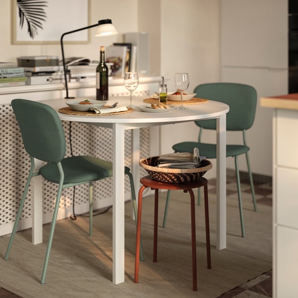 A round white dining table with four green chairs, set with wine and glasses, in a stylish kitchen.